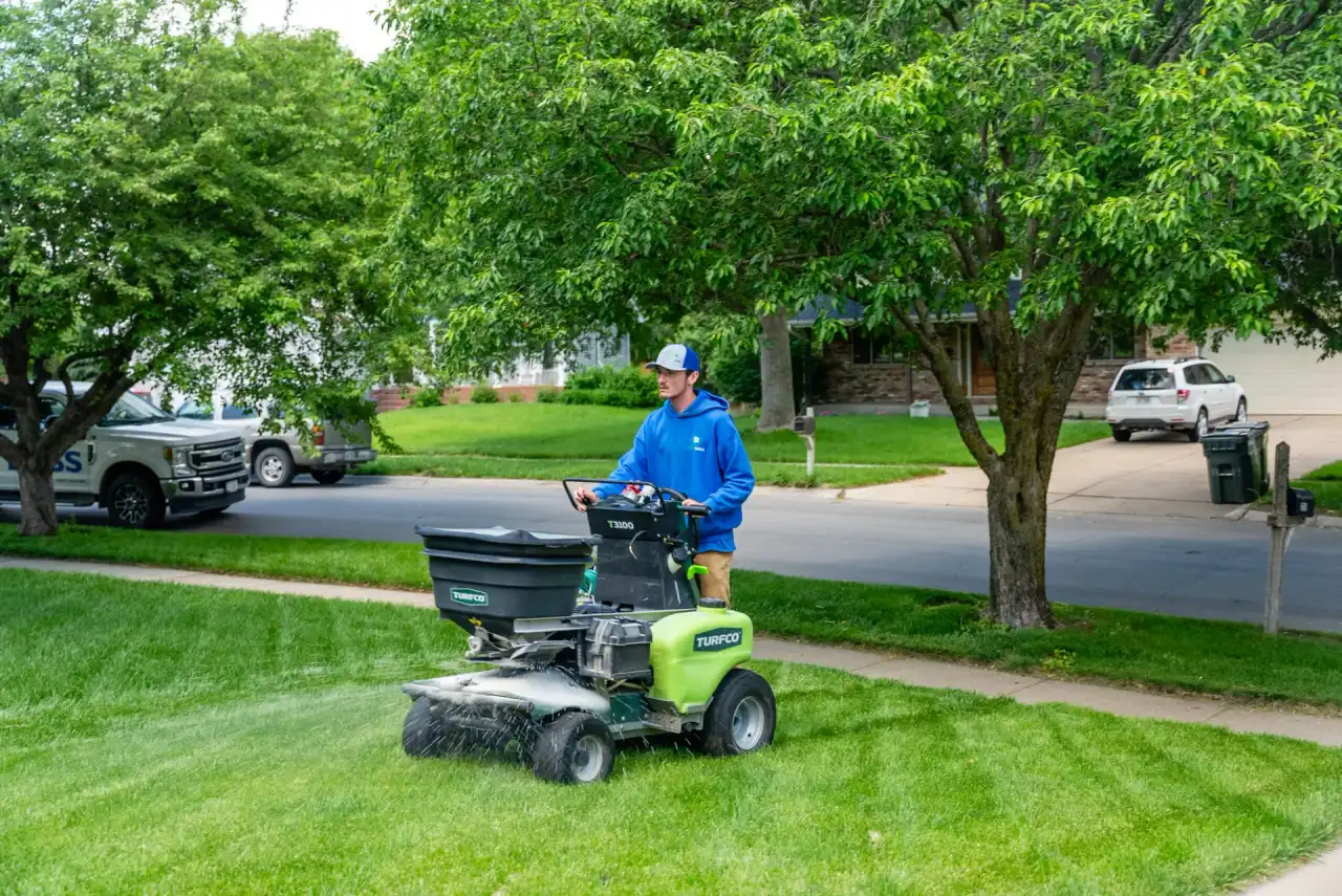 A Yard Boss technician applying a granular lawn treatment with a ride-on spreader on a residential front lawn in Lincoln, Nebraska