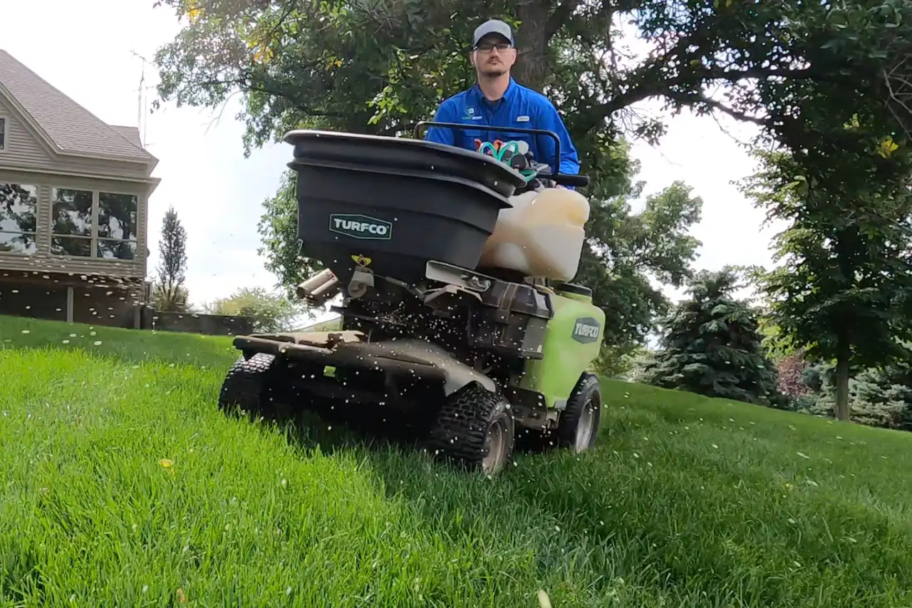 Close view of a Yard Boss spreader broadcasting granular fertilizer across a Nebraska lawn
